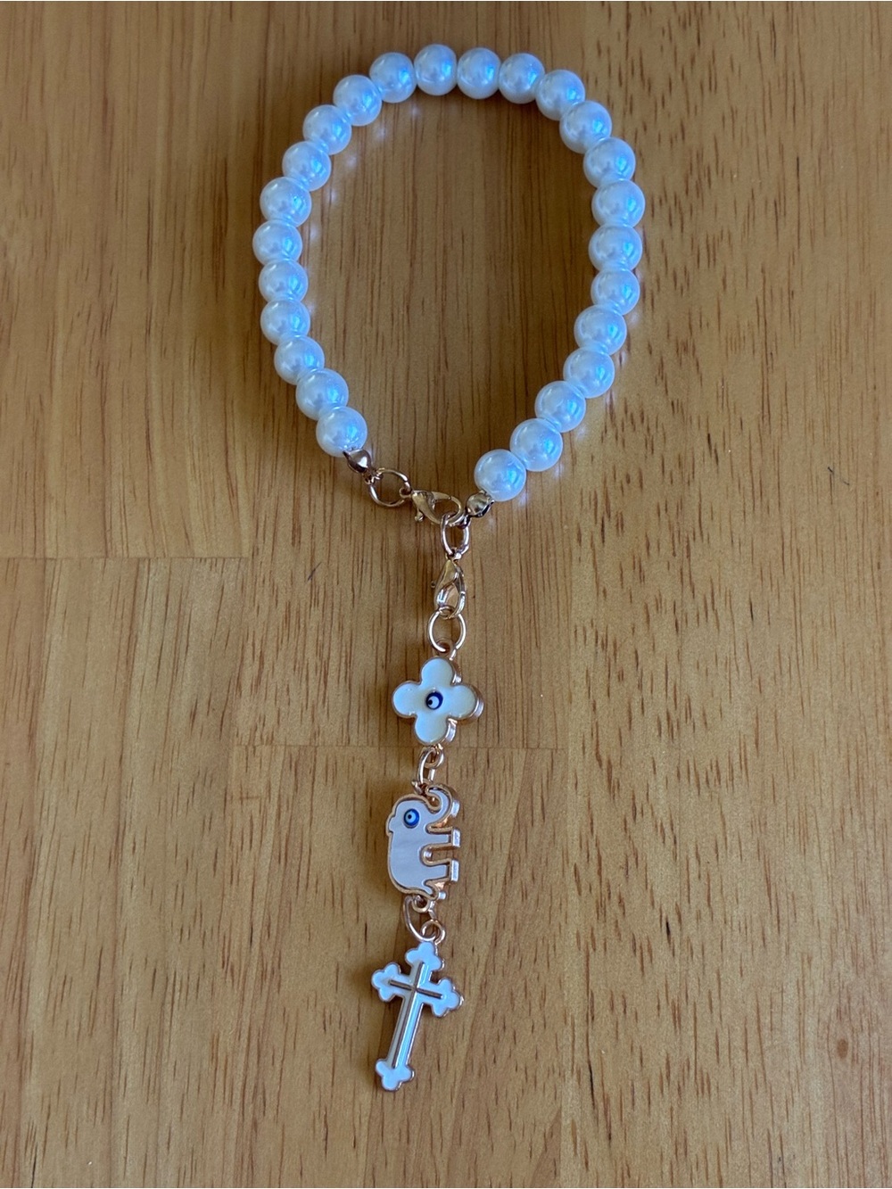 This white bead bracelet features a gold-tone cross, elephant and clover charm.